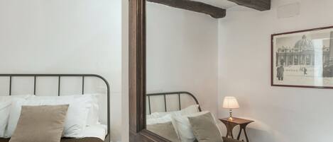 A bedroom with a bed, pillows, a bedside table with a lamp, and a framed picture on the wall.