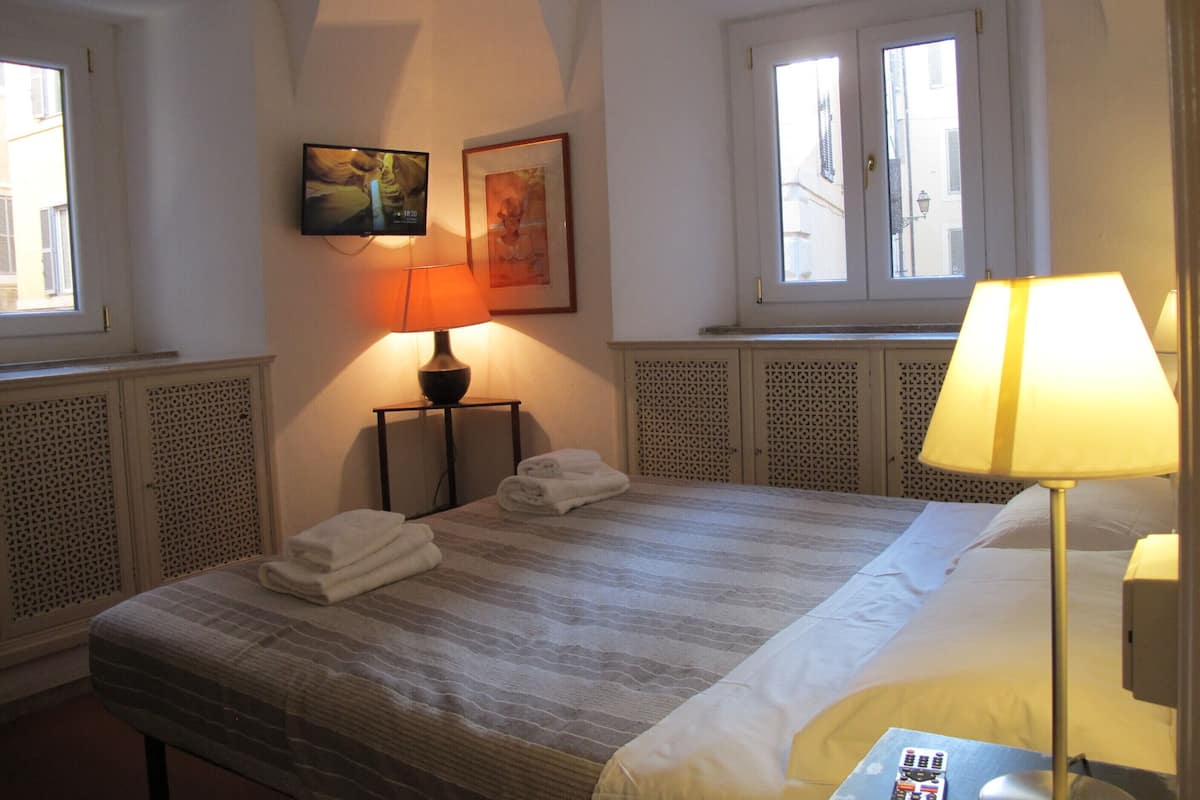 A hotel room with a bed, two bedside lamps, a TV, and a window with a view.