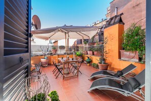 A rooftop patio with a table, chairs, an umbrella, and potted plants. - Arco in Pantheon Apartments (Rome)