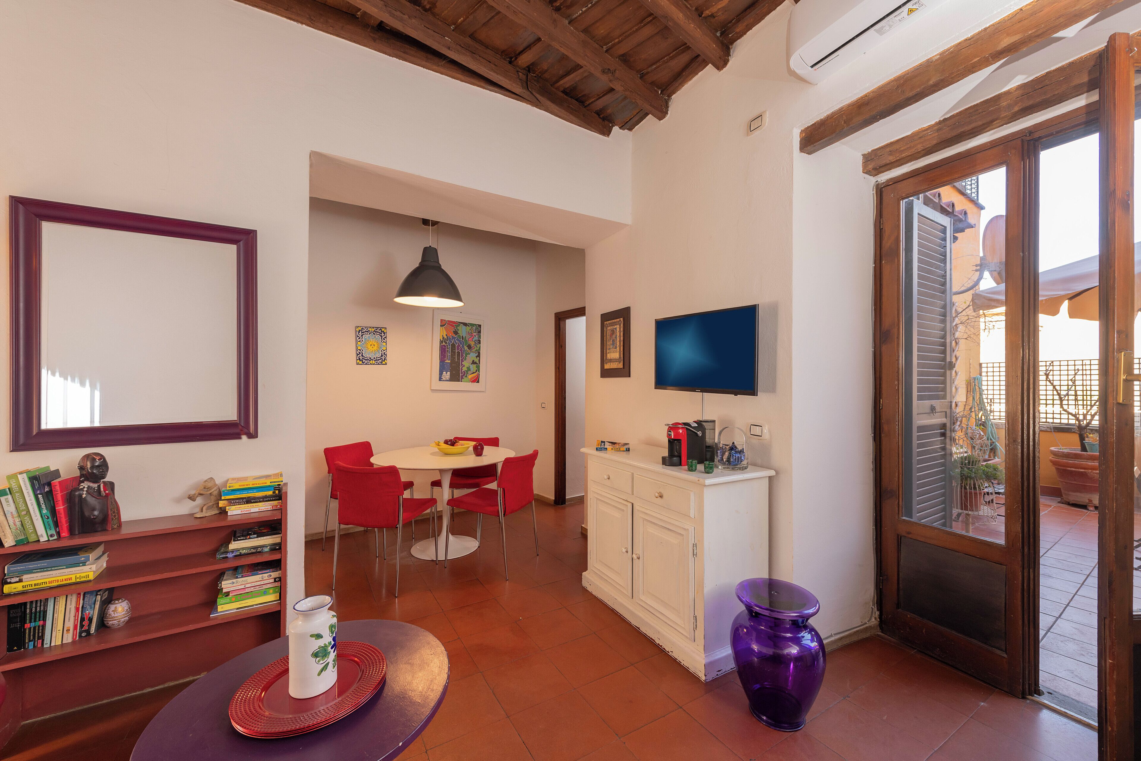 A room with a dining table, chairs, a bookshelf, a television, and a door leading to an outdoor area.