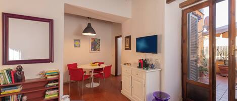 A room with a dining table, chairs, a bookshelf, a television, and a door leading to an outdoor area.