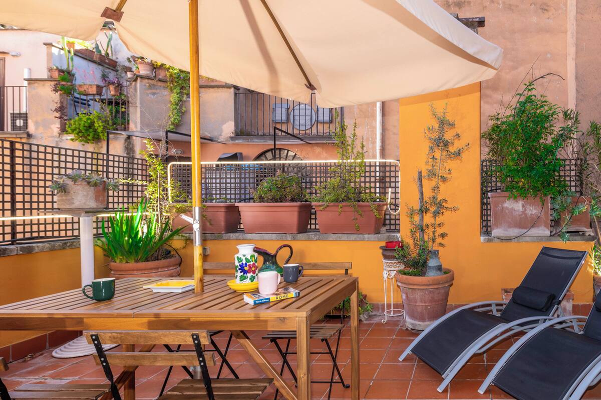 A wooden table with chairs, a potted plant, and a book titled 'ROME' under a canopy.