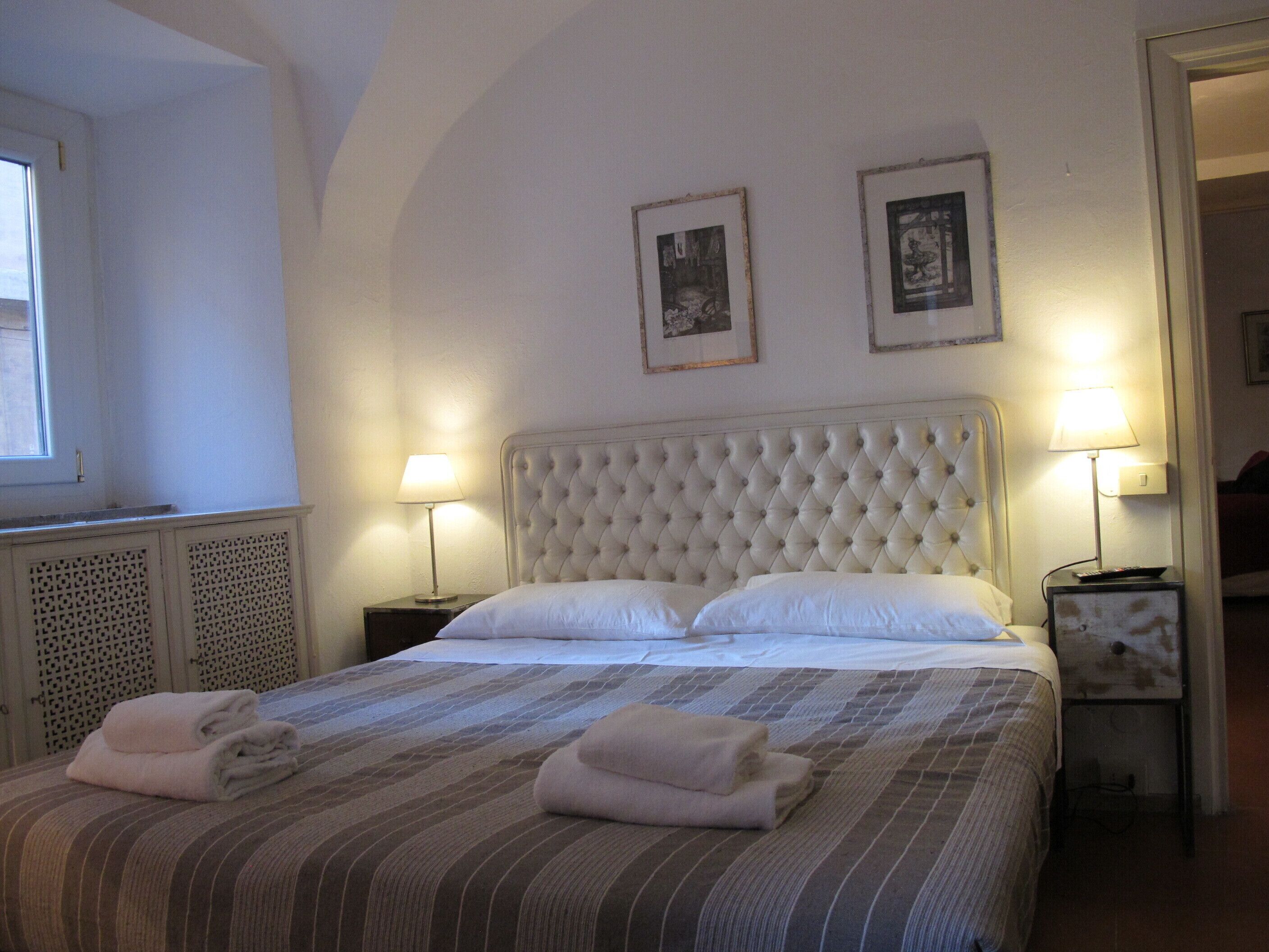 A hotel room with a large bed, two bedside lamps, and two framed pictures on the wall.