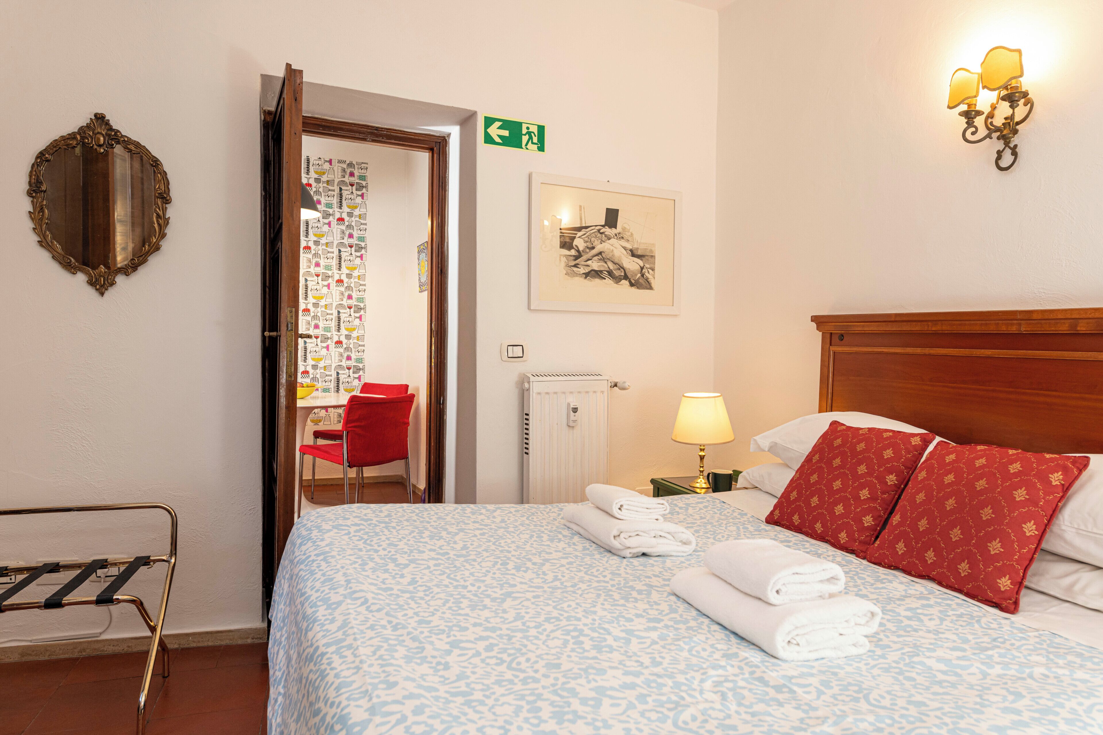 A hotel room with a bed, a red chair, a wall-mounted light fixture, and a framed picture.