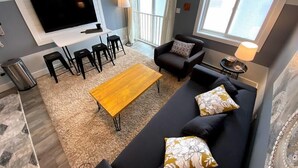 Un salon moderne doté d’un téléviseur à écran plat, de canapés noirs, d’une table basse en bois et d’un coin repas avec des tabourets noirs.