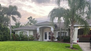A residential house with a well-maintained lawn, palm trees, and a garage. - Beautiful Private Florida Pool Home (Cape Coral)