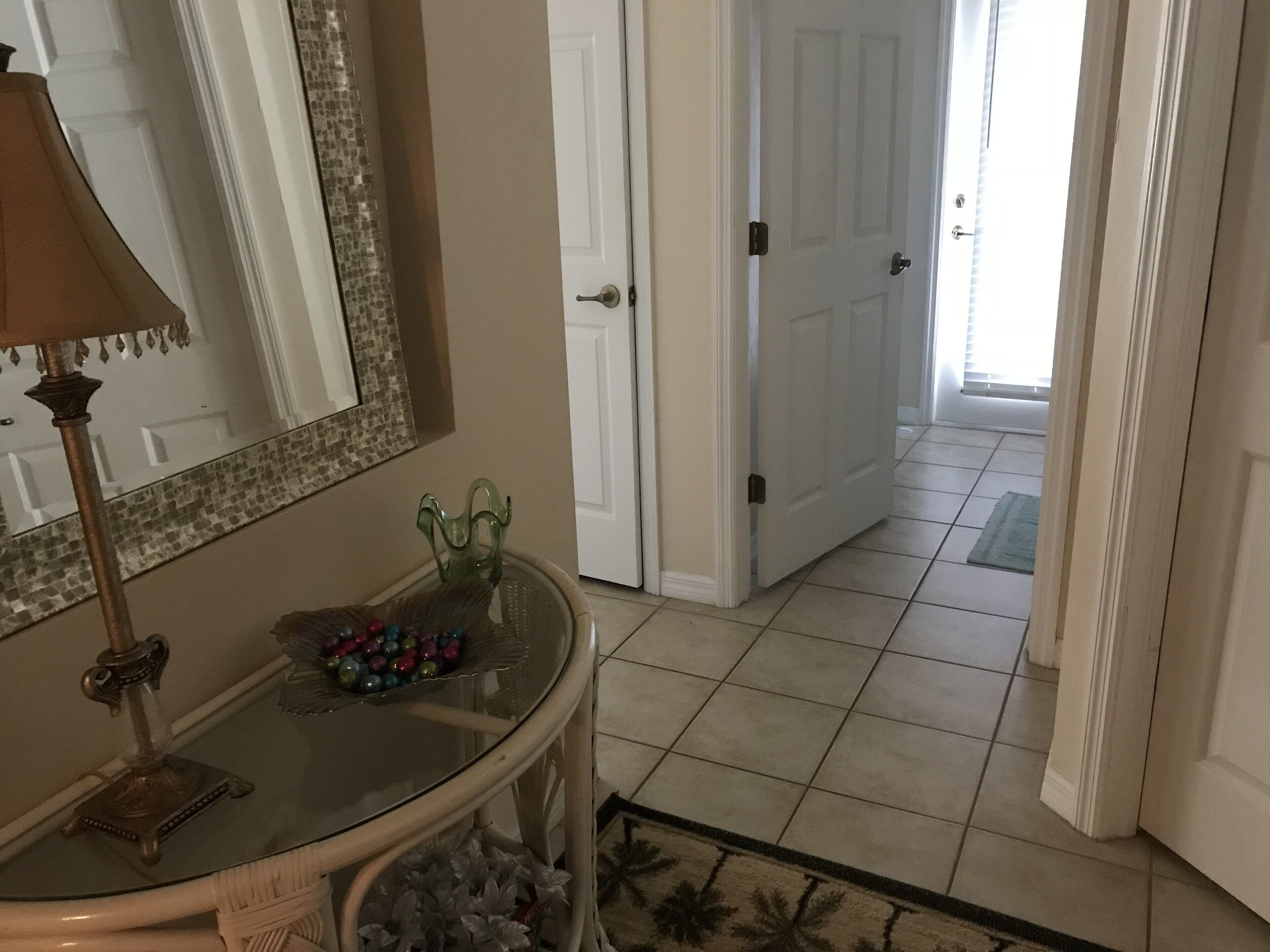 A bathroom with a glass vanity, a decorative mirror, and a door leading to another room.