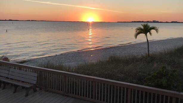 A sunset over a calm sea with a wooden deck and a bench. - Beautiful Private Florida Pool Home (Cape Coral)