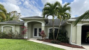 A residential house with a well-maintained lawn, palm trees, and a garage. - Beautiful Private Florida Pool Home (Cape Coral)