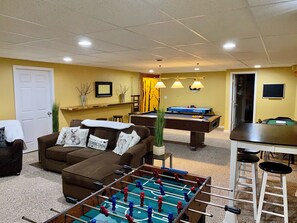 Un salon confortable avec un baby-foot, un canapé et une table de billard.