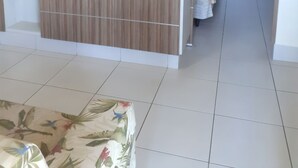 A modern living room with a flat-screen TV mounted on a wooden panel wall, a sofa with a floral pattern, and a tiled floor. - Flat Lacqua Diroma III - Um Verdadeiro Resort!!! (GO)
