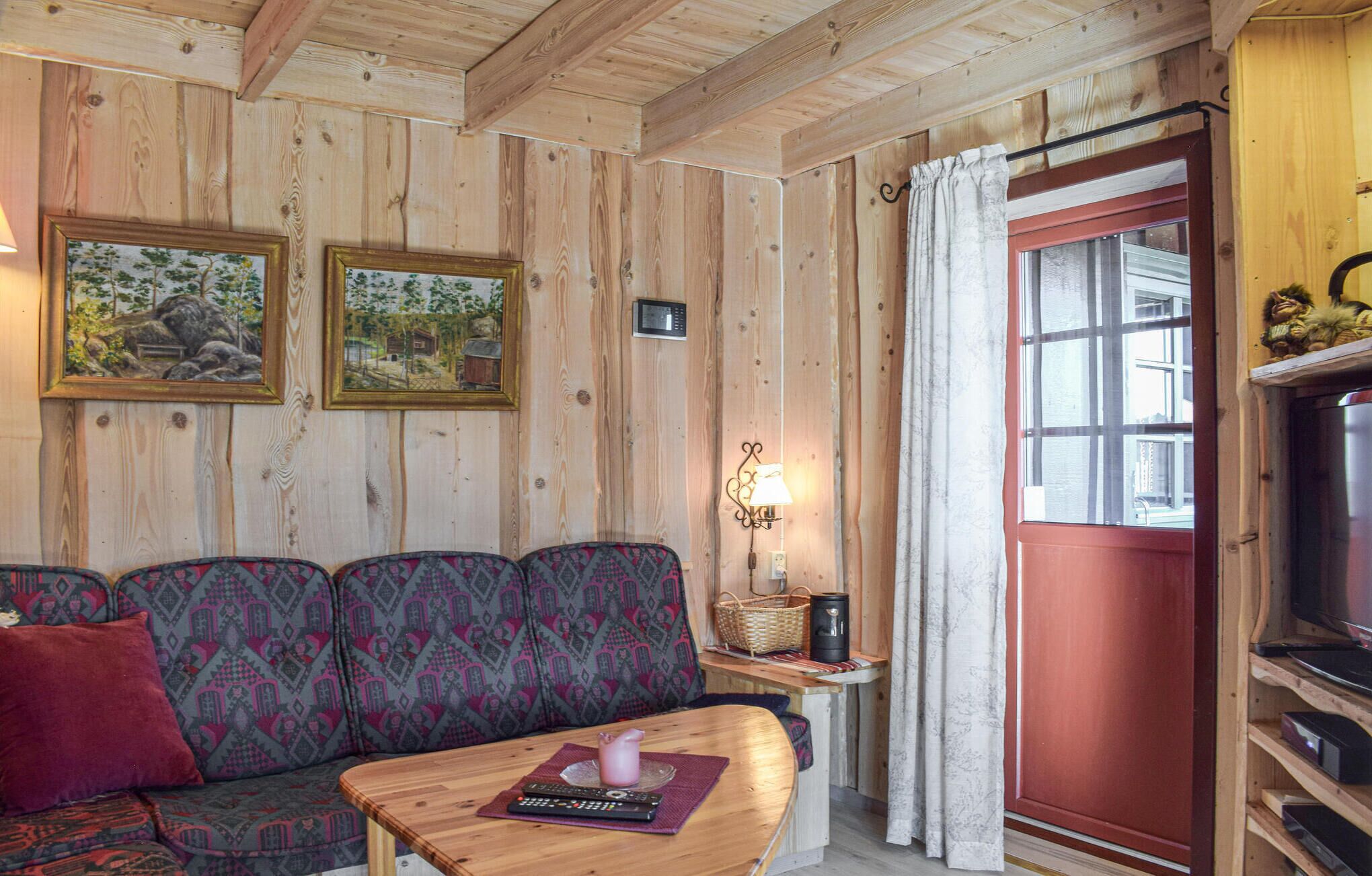 En inredning med träpanel, en soffa, ett litet bord med en fjärrkontroll, en lampa och en röd dörr.