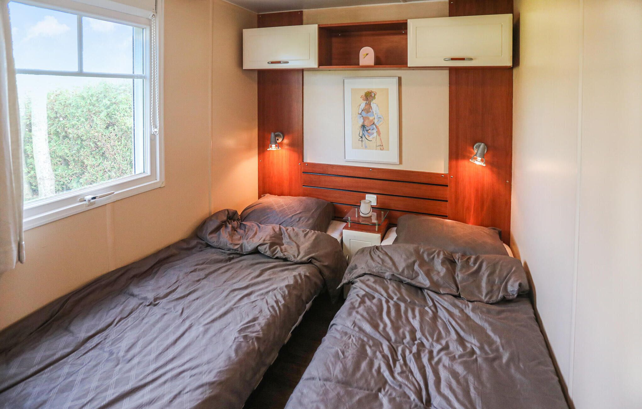 A small bedroom with two single beds, a bedside table with a lamp, and a framed picture on the wall.