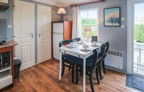 Een kleine keuken met een koelkast, een eettafel voor vier personen en een raam met uitzicht op groen.