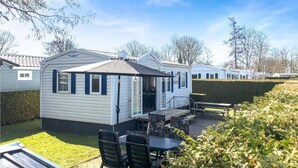 Une maison mobile dotée d’un patio, d’un espace salon couvert et d’un petit jardin.