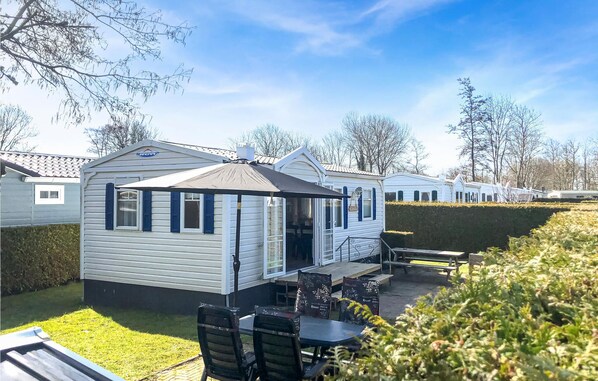 Een stacaravan met een terras, een overdekte zithoek en een kleine tuin.
