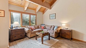 Una sala de estar acogedora con techo de madera, un conjunto de sofá, una mesa de centro y una mesita de noche con lámparas.