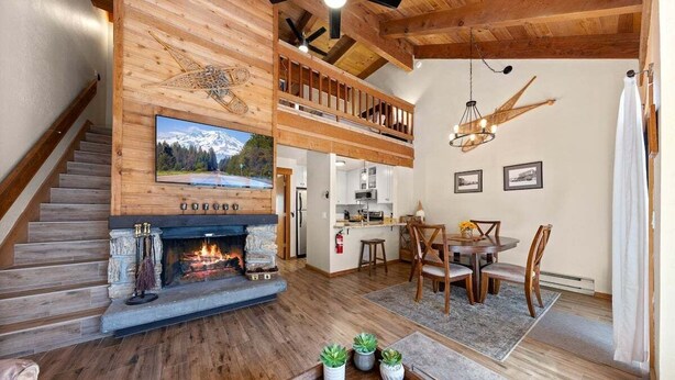 Un amplio salón con chimenea, suelo de madera, una mesa de comedor con sillas y una cocina al fondo.