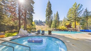Una piscina con hidromasaje, sillas de descanso y una zona cubierta, rodeada de árboles altos y cielo despejado.