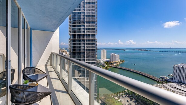 A balcony with two chairs and a view of a tall building and a body of water. - ICON W BRICKELL AMAZING OCEAN VIEW 2BR/1BA (Miami)