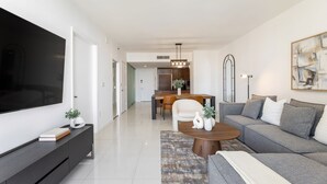 A modern living room with a flat-screen TV, a sofa, a coffee table, and a dining area with a chandelier. - ICON W BRICKELL AMAZING OCEAN VIEW 2BR/1BA (Miami)
