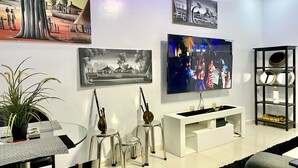 Un salon moderne avec un canapé blanc, une table basse en verre, un téléviseur fixé au mur et un tableau en noir et blanc encadré.