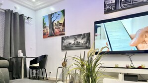 Un salon moderne avec un téléviseur à écran plat, une table à manger agrémentée d’un vase de plantes, un canapé et un fauteuil.