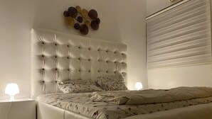 Une chambre à coucher avec une tête de lit capitonnée, une literie à motifs floraux, deux lampes de chevet et un élément décoratif mural.