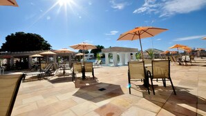 An outdoor patio area with sun umbrellas, lounge chairs, and a pool in the background. - Lindo Flat Localizado no Lacqua Diroma V (GO)