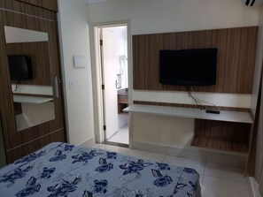 Quarto com cama, televisão fixada na parede e guarda-roupa com espelho.