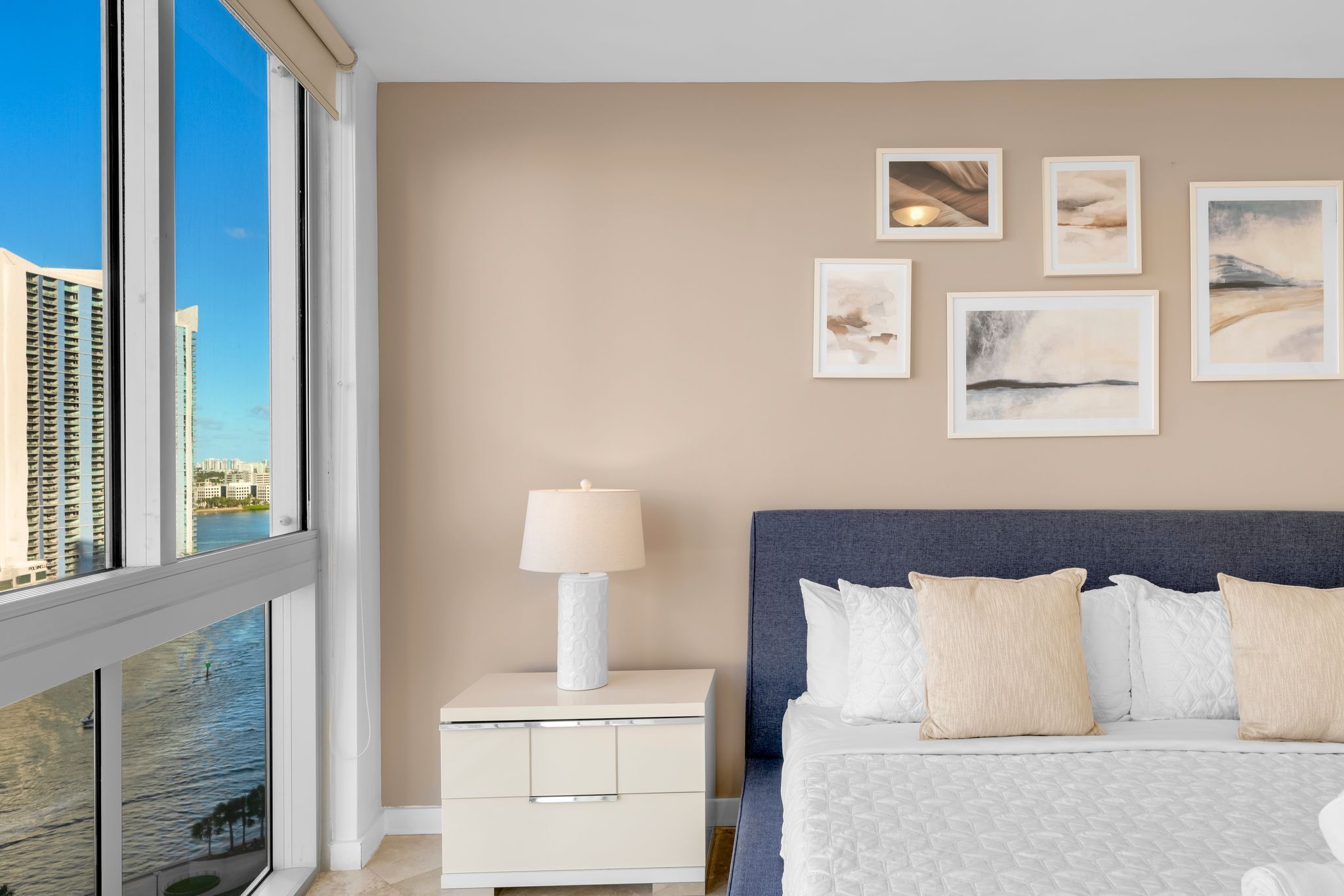 A modern hotel room with a large bed, a nightstand with a lamp, and artwork on the wall.