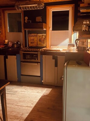A kitchen with a stove, refrigerator, and a window with blinds.