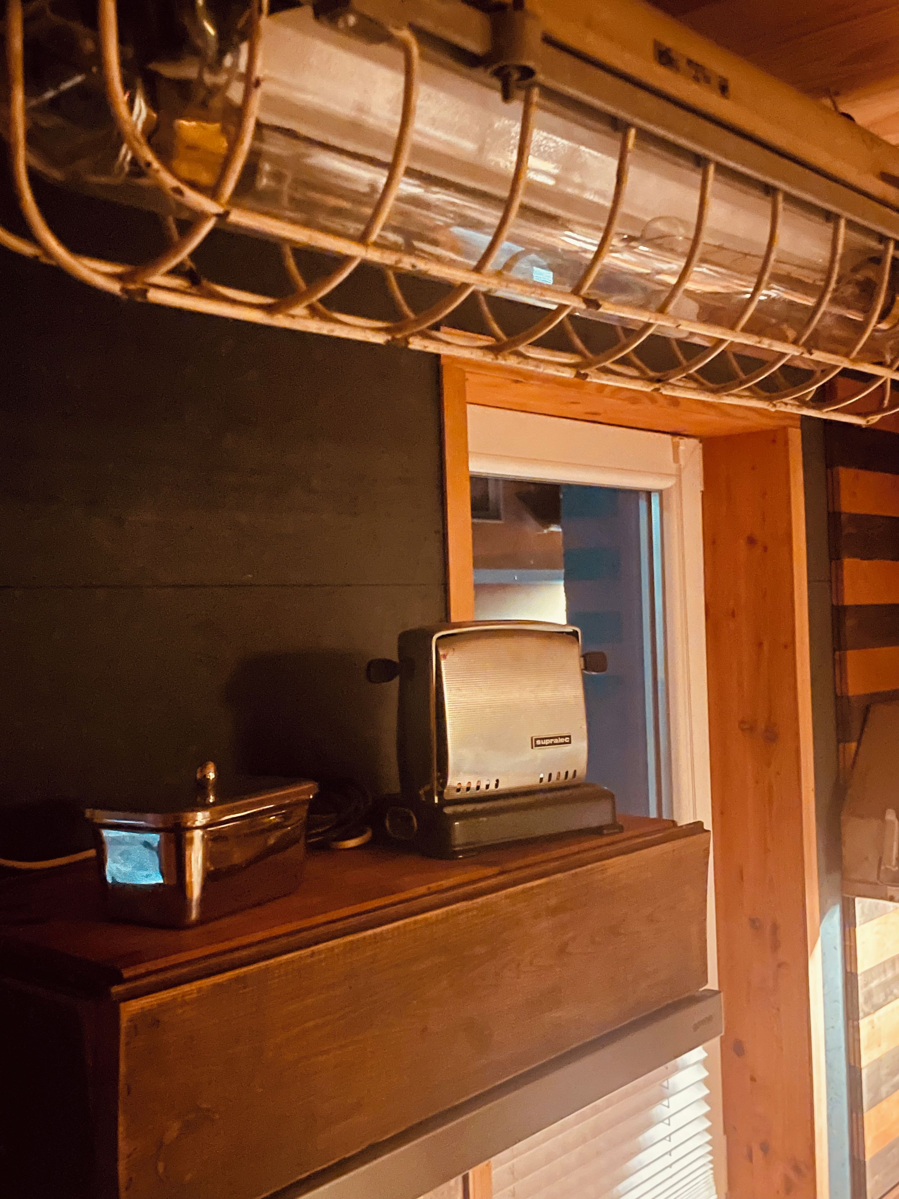 A kitchen with a toaster on a wooden counter, a window with blinds, and a ceiling vent.