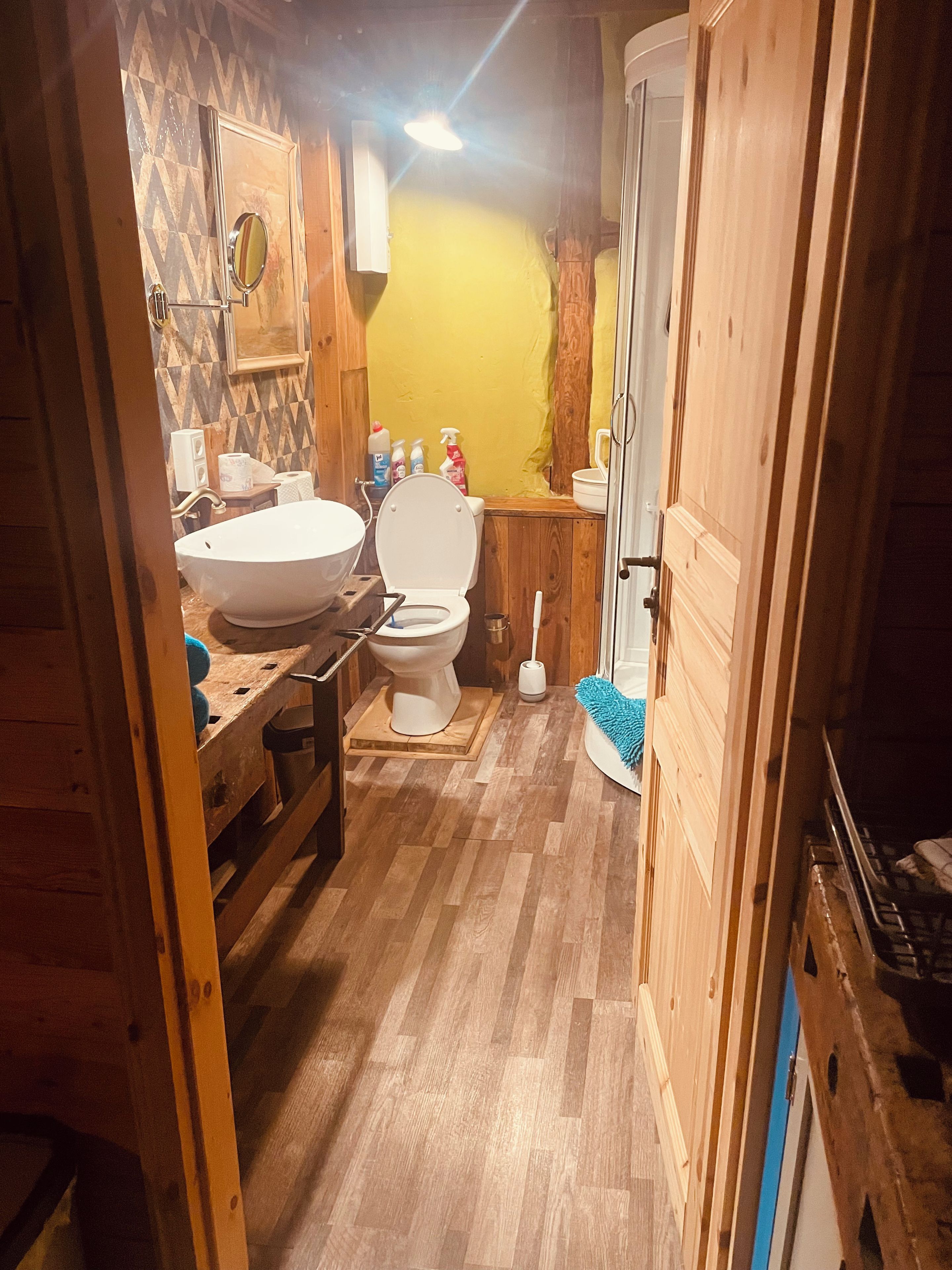 A wooden-floored bathroom with a white sink, toilet, and a mirror.