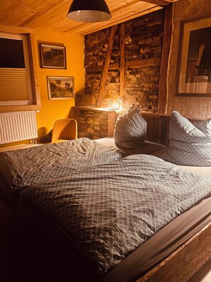 Un dormitorio con techo de madera, una cama con ropa de cama estampada, un escritorio con lámpara y una pared de piedra.