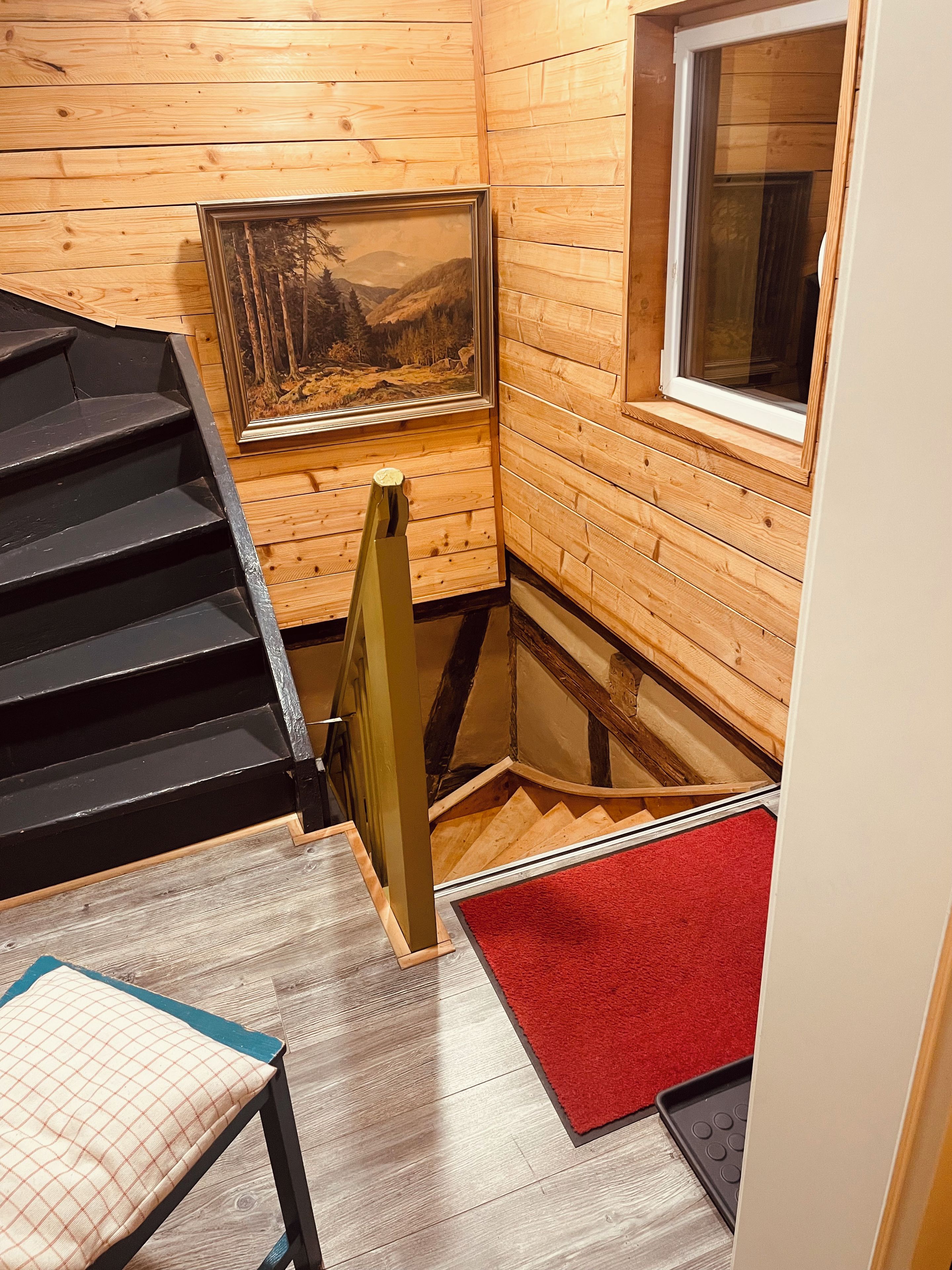 Ein Holzblockhaus-Interieur mit einer Treppe, einem gerahmten Landschaftsbild und einem Fenster.