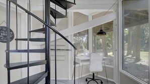 A modern interior with a spiral staircase, a desk with a chair, and a large window offering a view of the outdoors. - PEACEFUL SEABROOK ISLAND TREEHOUSE WITH LAGOON VIEWS (Seabrook Island)