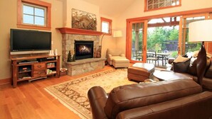 A living room with a fireplace, leather sofa, television, and a dining area with outdoor seating. - EV Charger! HOT TUB! Perfect family getaway in the ❤️ of Suncadia! (Cle Elum)
