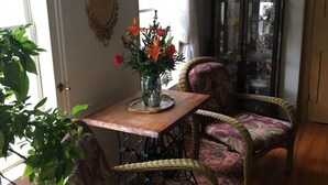 A dining area with a wooden table, two upholstered chairs, a vase with flowers, and a wicker chair. - Cooperstown Dreams Park Baseball Rental All Star Village Catskills Oneonta (Mount Vision)