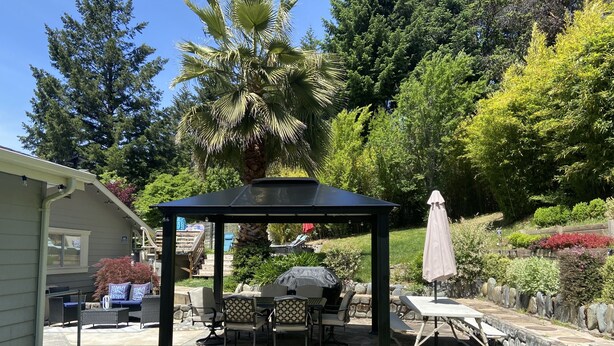 Ein überdachter Patio-Bereich mit Gartenmöbeln, einem Grill und einer Pergola.