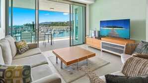 A modern living room with a large sliding glass door leading to a balcony with a view of a marina and boats. - 2 Bedroom (Whitsunday)