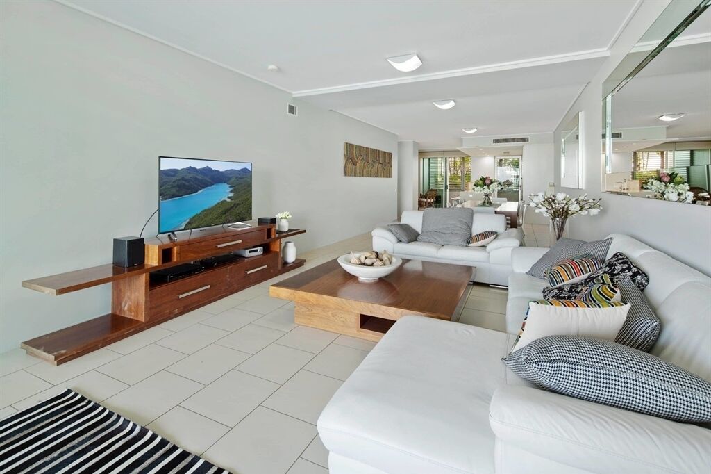 A modern living room with a flat-screen TV, a wooden entertainment unit, a white sofa, and a coffee table.