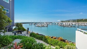 A marina with numerous boats docked, a modern building with a balcony overlooking the water, and a clear blue sky.