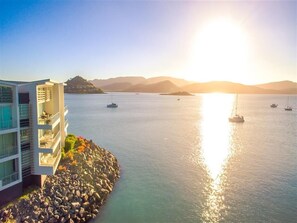 Ein Küstenhotel mit Blick auf das Meer und Boote, das ein modernes Gebäude mit Balkonen und eine felsige Küstenlinie zeigt.