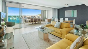 A modern living room with a yellow sofa, glass coffee table, and a view of a marina through large sliding doors.