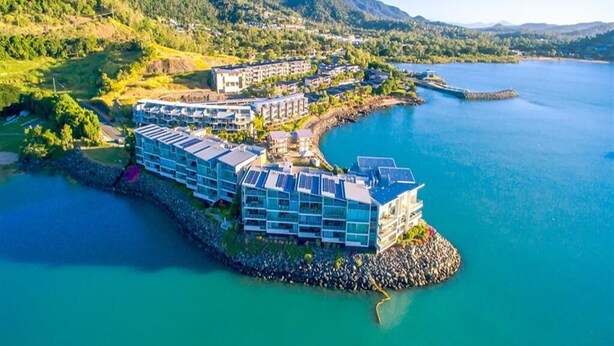 A coastal hotel with multiple buildings, a rocky shoreline, and a calm sea.