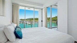 Habitación de hotel con una cama grande, vista al puerto deportivo y un balcón con puerta de vidrio.