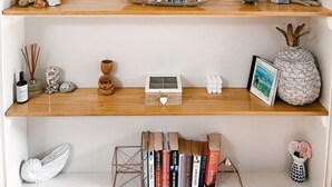 Une étagère bien rangée, ornée de divers objets décoratifs, notamment un panneau d’accueil, des livres et de petites sculptures.
