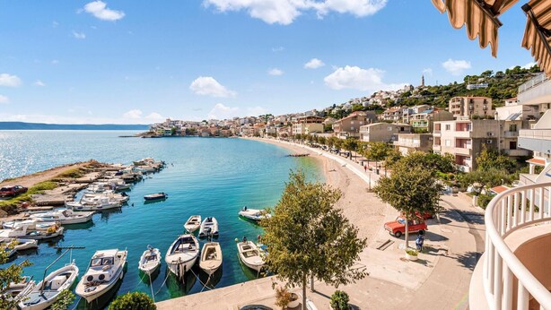 Un pueblo costero con un puerto deportivo, edificios a lo largo de la costa y un cielo azul despejado.