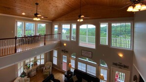 A spacious interior with wooden ceilings, multiple windows offering views of greenery, and a balcony with a railing. - Douglas Lake Waterfront Estate (Sevierville)